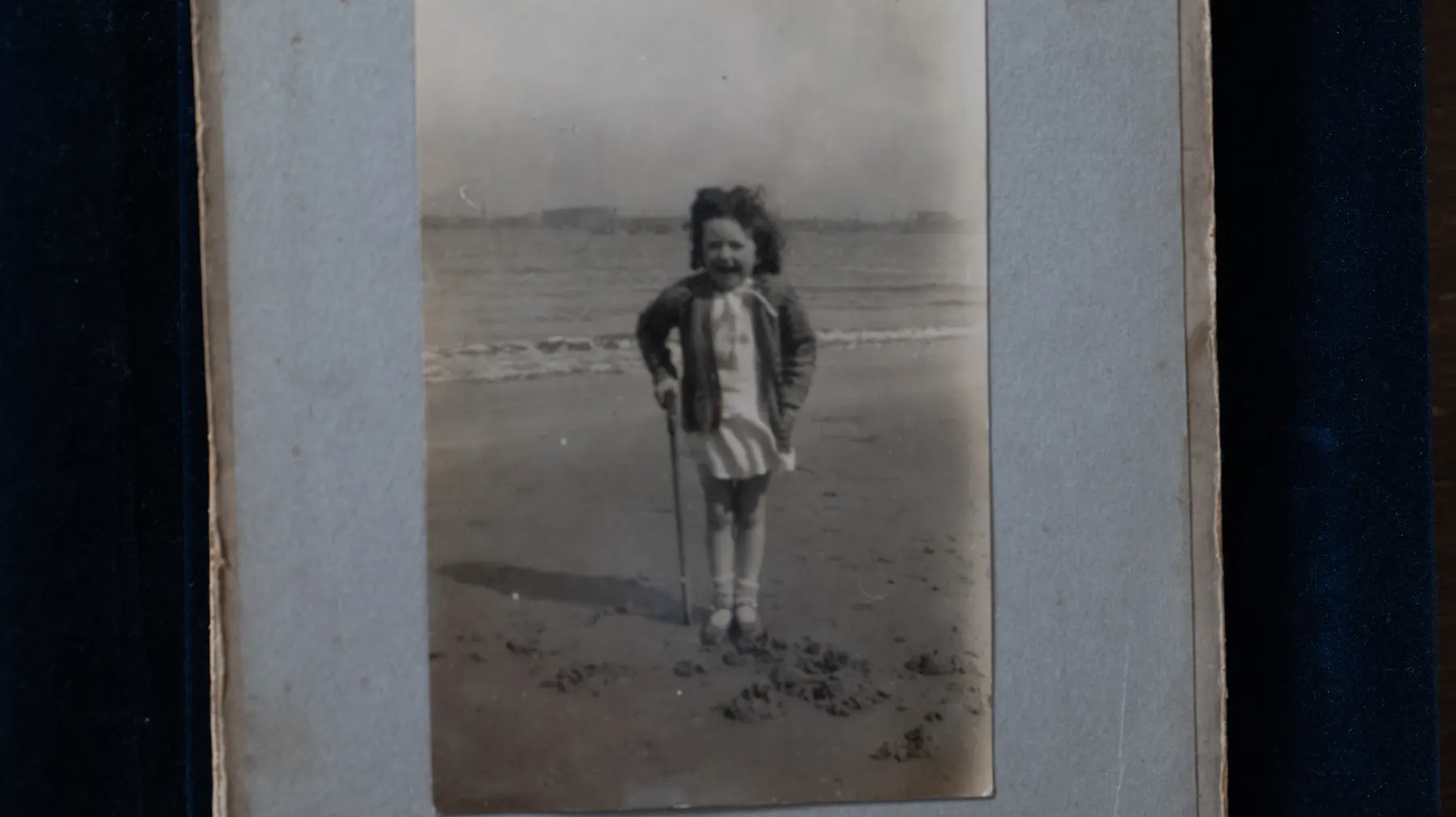 An old black and white photograph of a girl on a beach, in a family album