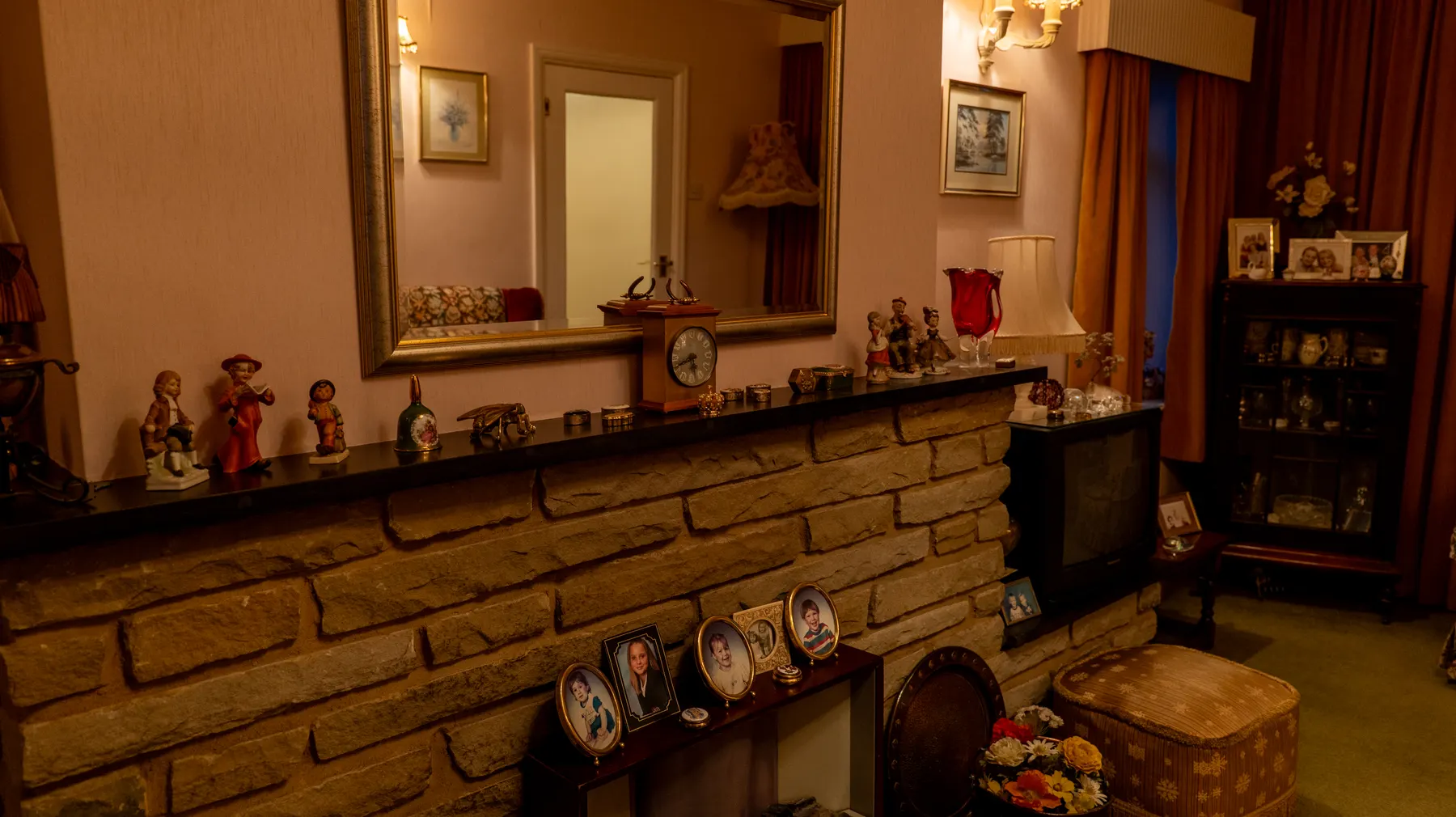 A living room at dusk, lamps lit, photographs on every surface