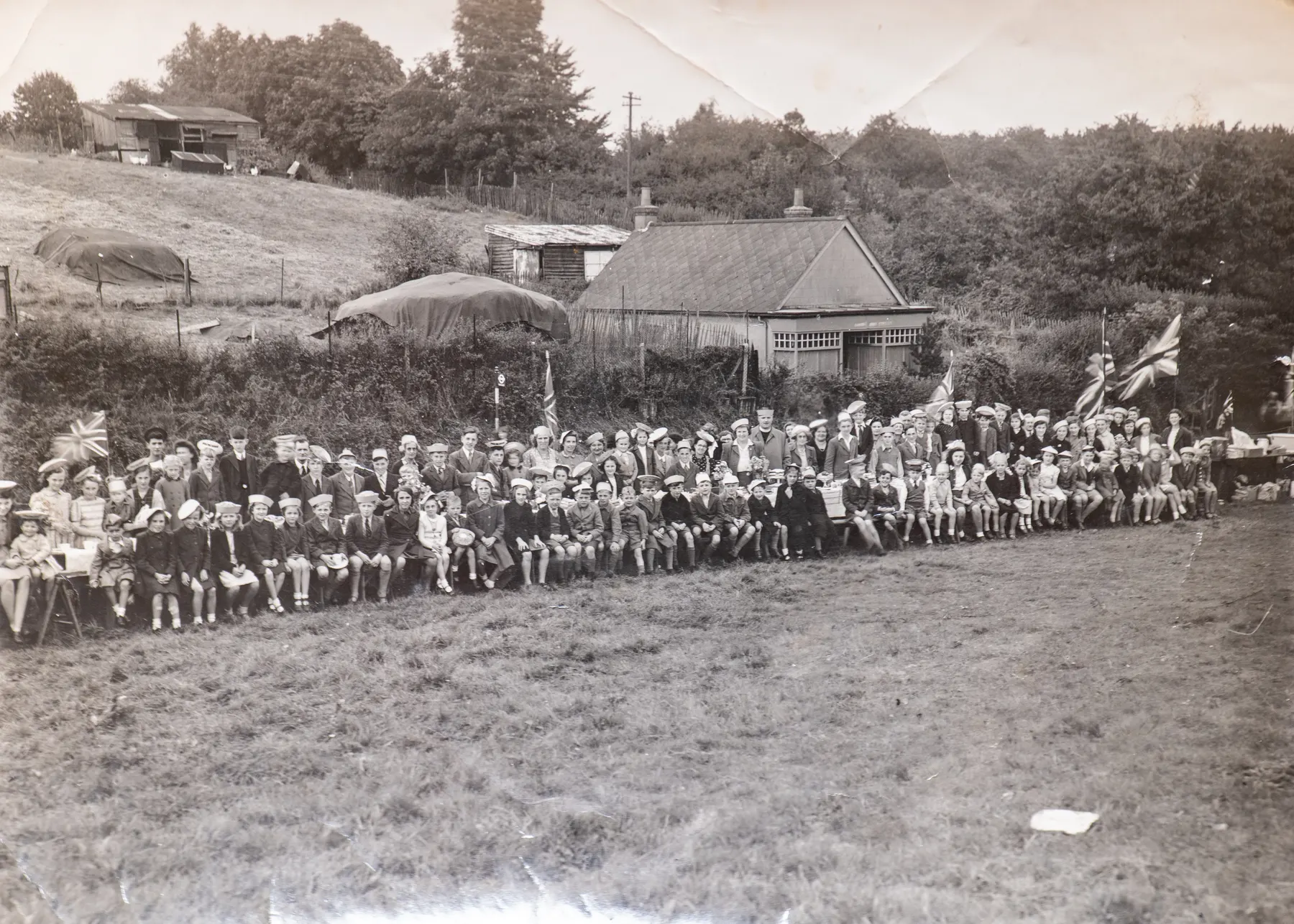 A 1945 street party photograph: rows of children at long tables in a field, bunting overhead